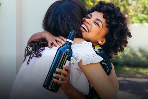 Two women hugging holding a bottle of wine